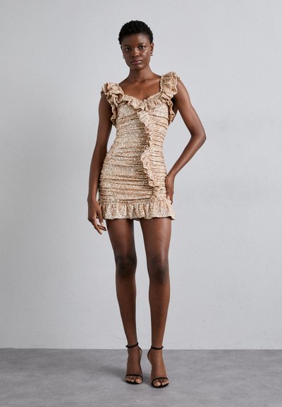 Robe mini dorée scintillante avec des bretelles volantées et un design froncé, arborant un ourlet volanté et un tissu texturé. Sandales à talons hauts noires.