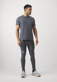 Sportos szürke rövid ujjú póló fekete logóval, szürke leggings-szel és ezüst futócipővel párosítva. Sima anyag, testhezálló fazon, minimális díszítéssel.
