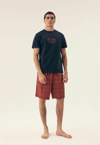 Granatowa bawełniana koszulka z nadrukiem "Malibu Beach"; czerwono-białe szorty w kratę z elastycznym pasem, o luźnym kroju i prostym fasonie.