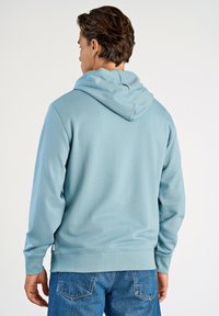 Sudadera azul claro con una capucha espaciosa, puños y dobladillo de canalé, hecha de una tela suave. Combinada con jeans de mezclilla azules. Diseño limpio; sin logotipos visibles.