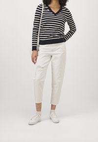 Navy and cream striped V-neck sweater, white distressed cropped jeans, and white sneakers, with a textured knit and minimal detailing.