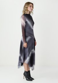 Długo rękawowa szara sukienka z marszczoną górą i warstwową spódnicą. Posiada przejrzyste rękawy i asymetryczny dół. W zestawie z czarnymi botkami na obcasie.