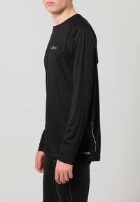 Svart långärmad träningsskjorta i lätt och välventilerat material, med nätaccenter och reflekterande logodetaljer på framsidan.