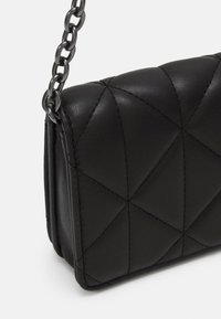 Sac à main noir matelassé en cuir lisse, doté d'une bandoulière en chaîne et d'une couture en forme de losanges, avec une forme rectangulaire compacte.