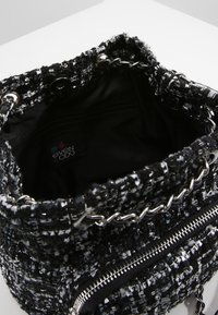 Sac à main tissé noir et blanc texturé avec des poignées en chaîne métallique et une poche zippée, doté d'un intérieur en tissu noir.