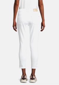 Jean blanc court avec une texture lisse, poches arrière, et une étiquette beige douce sur la ceinture, associé à des baskets neutres.