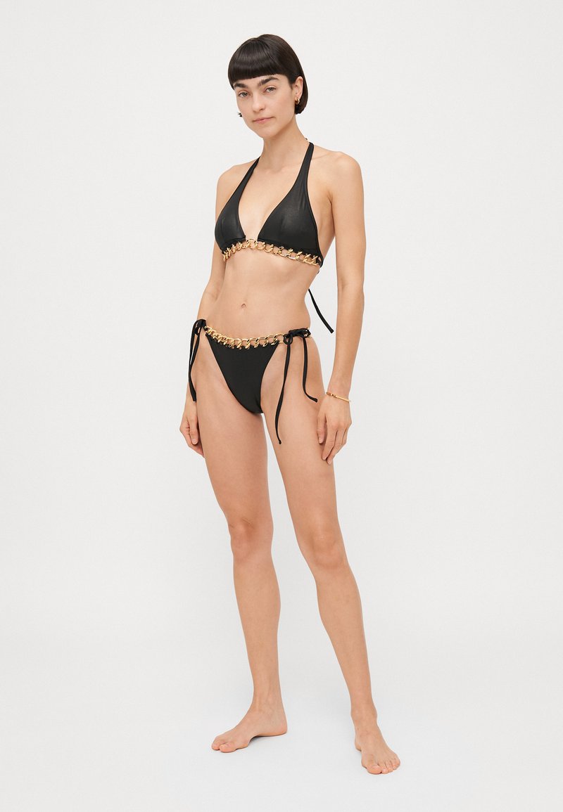Zwarte bikini met een halternek ontwerp. De bovenkant heeft een kettingaccent, terwijl de onderkant zijstrikken en een bijpassende kettingdetail heeft.