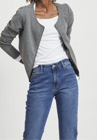 Gray textured bomber jacket with a round neckline, paired with blue high-waisted jeans. Jacket has a front zipper and fitted sleeves.