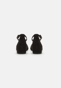 Sorte mokasiner i semsket skinn med lav hæl, med en bakre ankelrem og rund tå. Glatt tekstur og minimalistisk design.