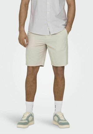 Herrens ljusbeige shorts med ett texturerat mönster, kombinerat med grön-grå sneakers och vita korta strumpor. Skjortan är ljusgrå och randig.