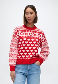 Suéter de punto rojo con patrones de corazones blancos y texto 'XOXO', con un cuello y puños acanalados, de textura suave y corte relajado.