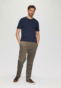 Granatowa koszulka z krótkim rękawem zestawiona z oliwkowymi spodniami sztruksowymi i brązowymi sneakersami, z zapięciem na sznurówki i białymi podeszwami.