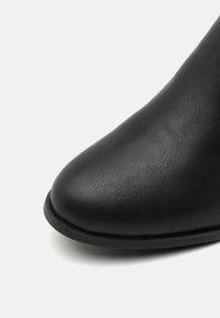 Botte chelsea en cuir noir avec un bout arrondi et une texture lisse. Présente une semelle en caoutchouc plate et basse et des coutures discrètes le long du bord.