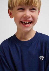 Marinblå kortärmad T-shirt med rund halsringning och ett litet broderat emblem på bröstet. Slät textur, avslappnad passform.