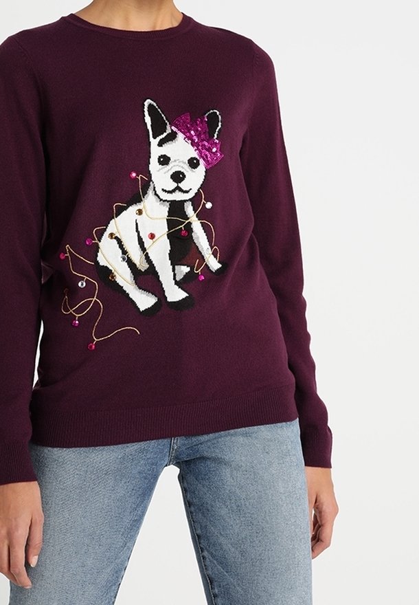 Burgundy neulepaita, jossa on valkoisen koiran grafiikka, sequin-ristiä pinkillä nauhalla ja värikkäillä koristekielillä. Klassinen pyöreä kaula-aukko.