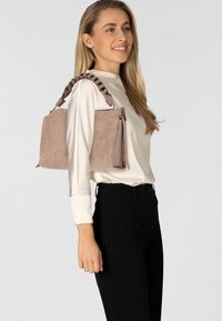 Sac en daim taupe de forme rectangulaire, avec une bandoulière tressée, des accroches en argent et une texture lisse.