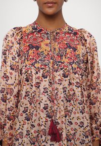 Blumenbluse aus leichtem rosafarbenem Stoff. Mit lebhaftem roten, lila und gelben Blumenmuster. Lockere Passform mit Quastendetail und gefaltetem Frontbereich.
