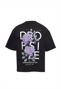 T-shirt noir présentant de grandes roses lavande sur des lettres blanches en bloc et un texte blanc énumérant des villes dans une collection en édition limitée.