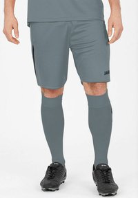 Pantaloni sportivi grigi con dettagli neri, realizzati in tessuto traspirante. Presentano il logo JAKO sulla gamba destra. Abbinati a calze grigie coordinate.