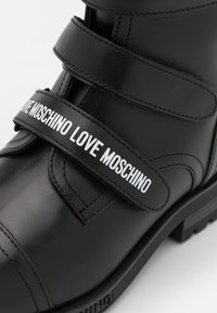 Zwarte leren laars met twee klittenbandbanden, waarvan één met "LOVE MOSCHINO" in witte tekst, en een dikke rubberen zool.