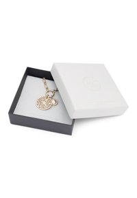 Bracelet doré dans une boîte à bijoux noire. Comprend un pendentif rond avec un texte gravé et un petit accent circulaire. La boîte a un couvercle texturé blanc.