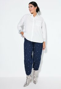 Witte overhemden met een borstzak, gecombineerd met donkerblauwe broek versierd met witte parels, en zilveren enkellaarsjes met een spitse neus.