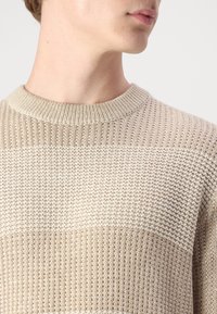 Maglione beige lavorato a maglia con righe verticali e orizzontali testurizzate. Presenta un collo a coste e un tessuto morbido e leggero.