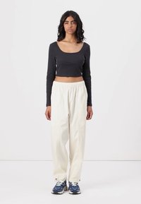Svart langermet crop topp kombinert med løstsittende kremfargede bukser og blå sneakers. Glatt stoff med en tettsittende design og elastisk midje.
