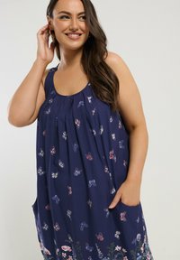 Marineblaues ärmelloses Kleid mit Schmetterlings- und Blumenmustern; hat Seitentaschen und Falten am Ausschnitt für zusätzliche Details.