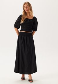 Svart tvådelat set bestående av en puffärmad cropped topp och en lång kjol, båda med samlad textur och elastiska detaljer.