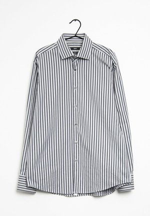 Herrelangærmet skjorte med knapper og lodrette sorte og hvide striber, hængende på en sort bøjle mod en hvid baggrund.