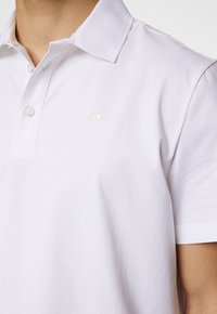 Vit polo skjorta med krage, två knappar och en liten ton-i-ton logotyp. Tillverkad av slät bomullsblandning. Korta ärmar.