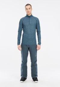 Maglia a maniche lunghe, blu, con collo a zip realizzata in un tessuto testurizzato, abbinata a pantaloni grigio scuro. L'outfit è completato da calzature nere.