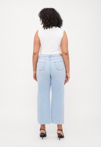 Light blue wide-leg jeans with raw hem, featuring a mid-rise waist and back pockets. Paired with a sleeveless white top and black heels.