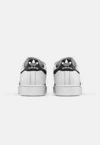 Biele tenisky Adidas z pohľadu zozadu, s čiernymi pätkami a logom Adidas a trojlístkom.