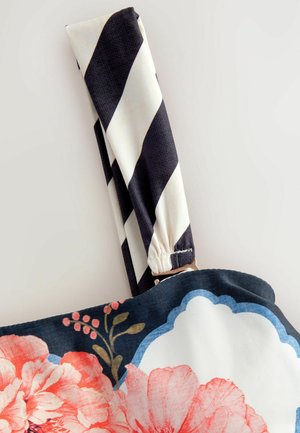 Blumenhandtasche mit dunkelblauem Grund, verziert mit pinken und weißen Blumen. Der Riemen ist schwarz-weiß gestreift und hat eine Hardware-Akzent in Goldfarbe.