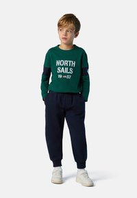 Grünes Langarmshirt mit weißem "NORTH SAILS 1957"-Aufdruck; marineblaue Jogginghose; weiße Sneaker; weicher, lässiger Stoff; lockere Passform.