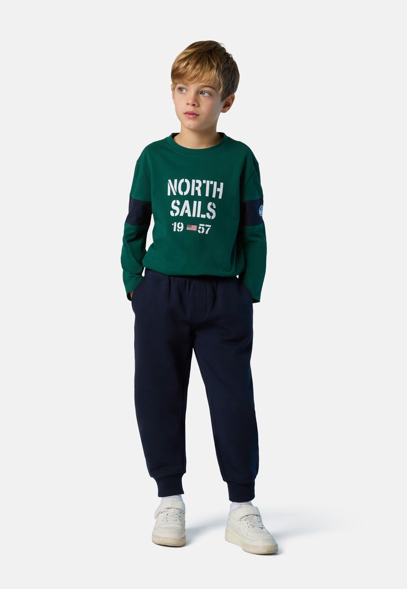 Grünes Langarmshirt mit weißem "NORTH SAILS 1957"-Aufdruck; marineblaue Jogginghose; weiße Sneaker; weicher, lässiger Stoff; lockere Passform.