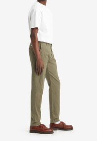 Olivgröna chinos med rak passform, tillsammans med en enfärgad vit t-shirt och bruna läderskor. Outfitten har avslappnade, texturerade tyger.