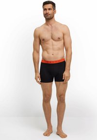 Boxer briefs neri con un elastico arancione in vita etichettato "FALKE". Il tessuto appare liscio e aderente, con un design semplice.