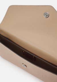 Béžová kožená peněženka s texturovaným vnějším povrchem, hladkým vnitřkem, uzávěrem na patent a malou popisnou značkou. Vnitřní prostor je neomezený.