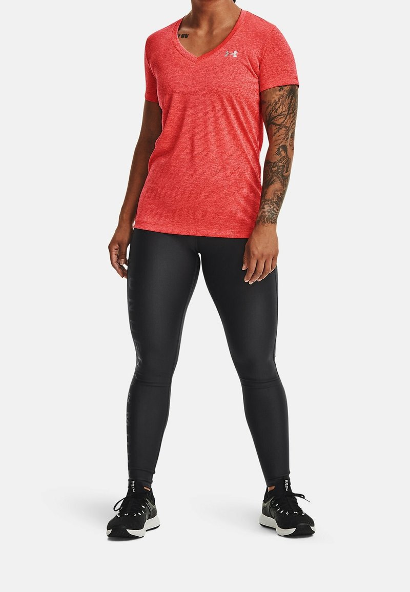 Red, textured short-sleeve V-neck shirt paired with black, form-fitting leggings and black athletic shoes with white soles.