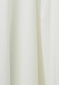 Rideau en tissu blanc avec des plis verticaux doux et une texture lisse, suspendu uniformément contre un fond neutre.