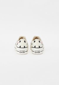 Tenisówki z płótna o białej podstawie, czarne w kropki i czerwone akcenty. Posiadają gumową podeszwę oraz branding "Converse All Star" na pięcie.