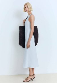 Ljust blå ärmlös midi-klänning, mjuk textur, i kombination med en stor brun vävd tote-väska och bruna sandaler med remmar.