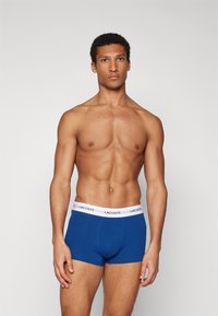 Boxer shorts en coton bleu avec une ceinture blanche portant le logo "LACOSTE", fabriqués à partir d'un tissu doux et extensible pour le confort.
