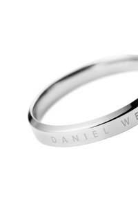 Bracciale in acciaio inossidabile argentato con superficie liscia e lucida e testo in rilievo "DANIEL WELLINGTON" su un lato.