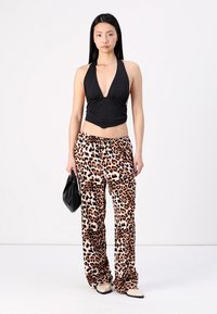 Haut halter noir avec un décolleté en V profond, associé à un pantalon ample imprimé léopard. Le mannequin porte un petit sac noir et des chaussures de couleur claire.