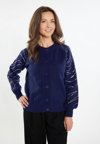Cardigan blu scuro con scollo rotondo, chiusura con bottoni e fili metallici decorativi a motivo ondulato sulle maniche. Polsini e orlo a coste.