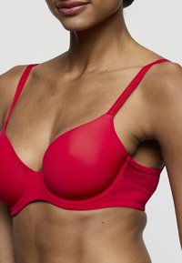Rode beha met gladde, gevormde cups; dunne verstelbare bandjes; naadloos ontwerp; zachte, rekbare stof; centrale band; veelzijdige en comfortabele pasvorm.